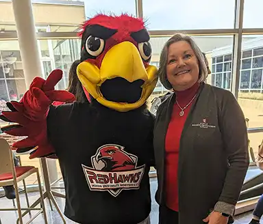 Dean, Cynthia S. Roberts, standing with the Redhawks mascot