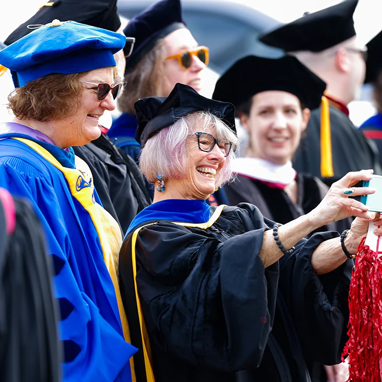 Two faculty members in robes smiling while taking a picture.