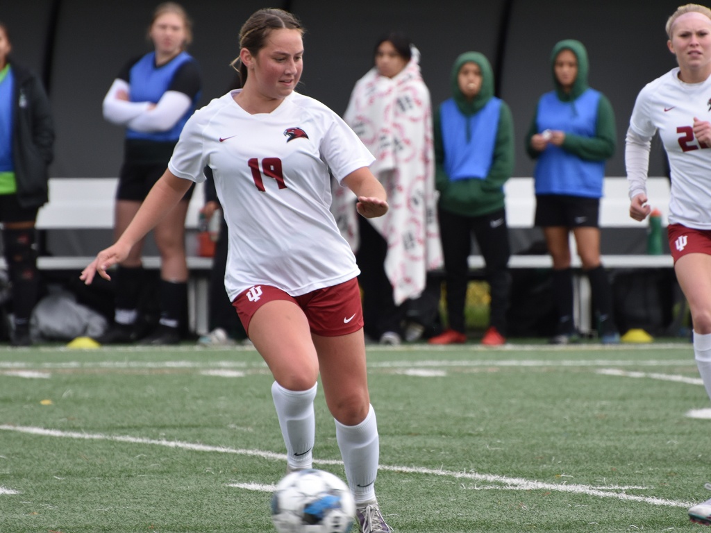 A women's soccer player kicks a ball.